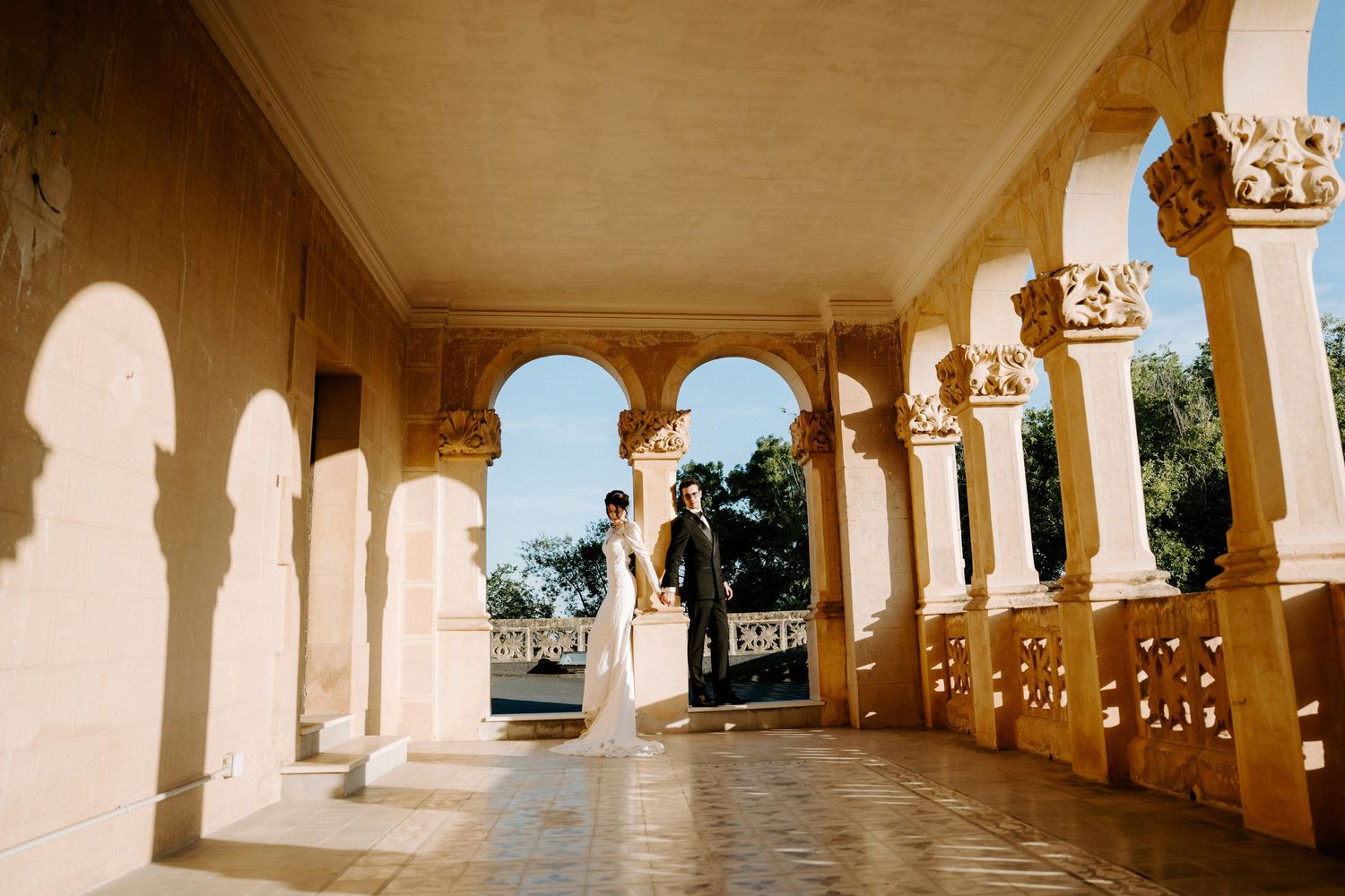 Long colonnade with ornate stone columns creates stunning wedding venue perspective.