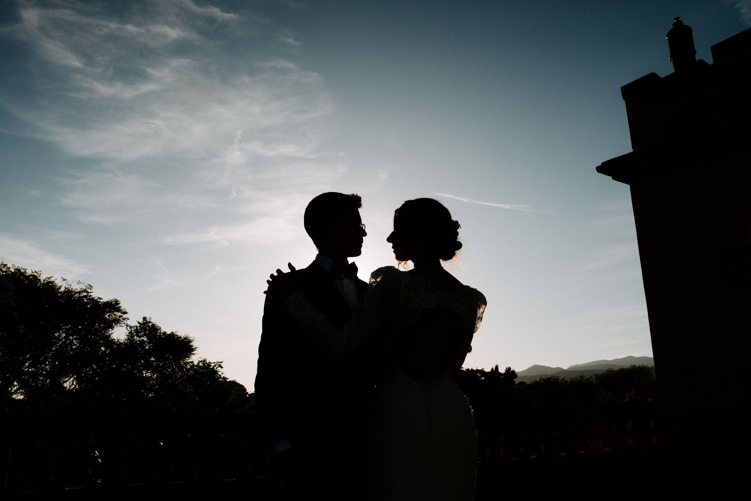 Silhouettes of wedding guests gathered at sunset against a dramatic sky.