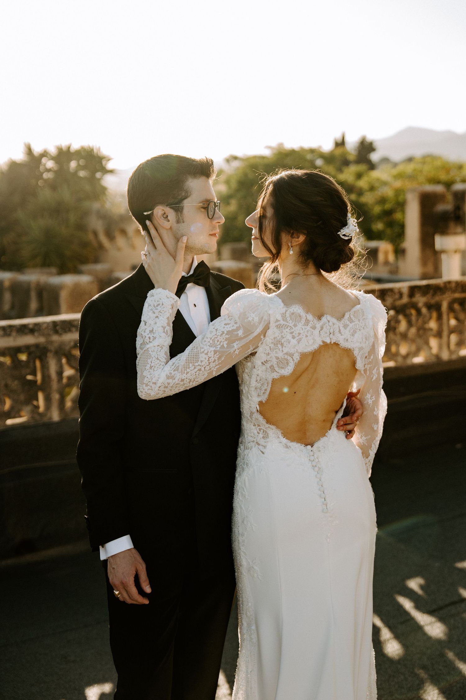 Elegant wedding couple embracing in beautiful natural light with lace dress details.
