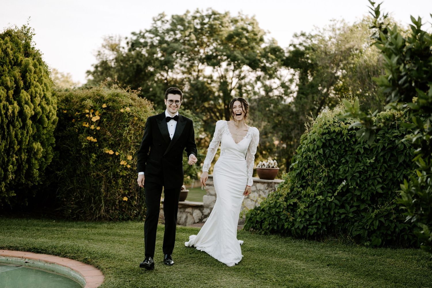 Wedding couple walking through a lush garden path surrounded by greenery.