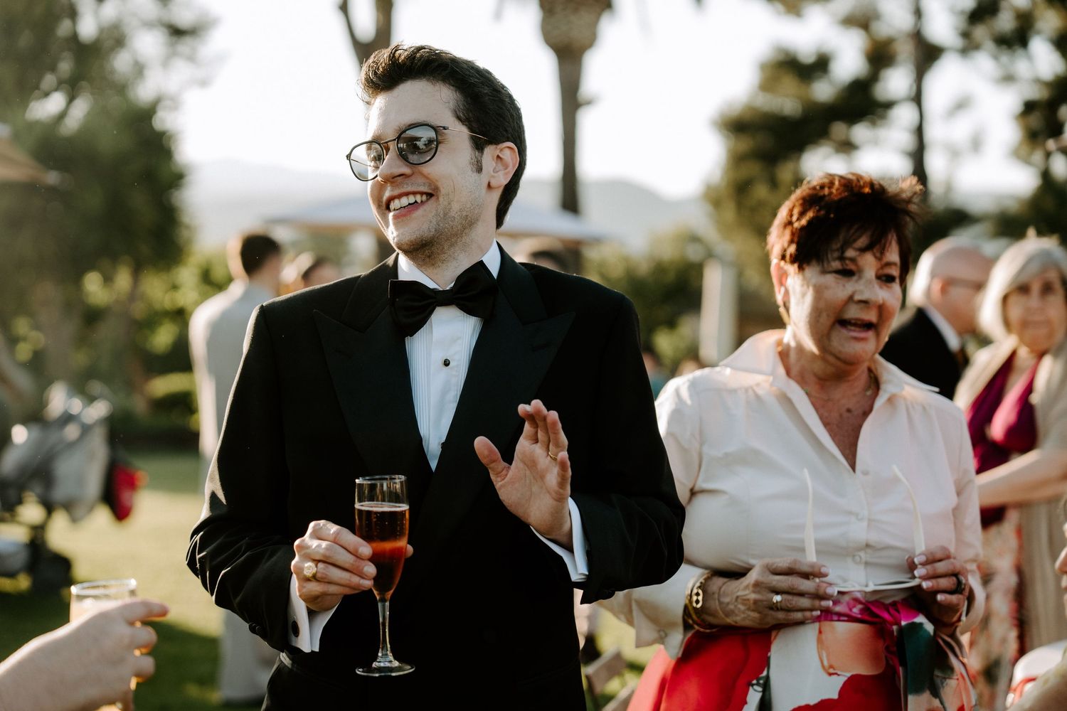 Wedding reception guests mingling outdoors with drinks at sunset.