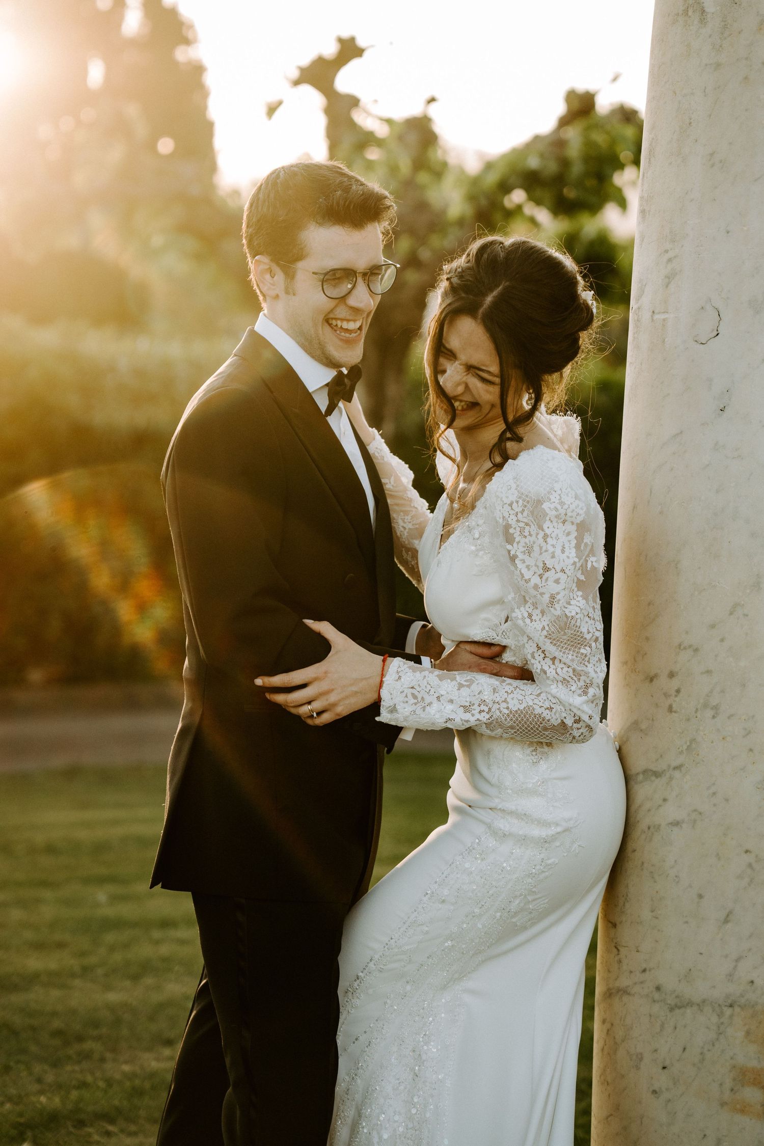 Sunset wedding portraits with couple laughing against white pillars.