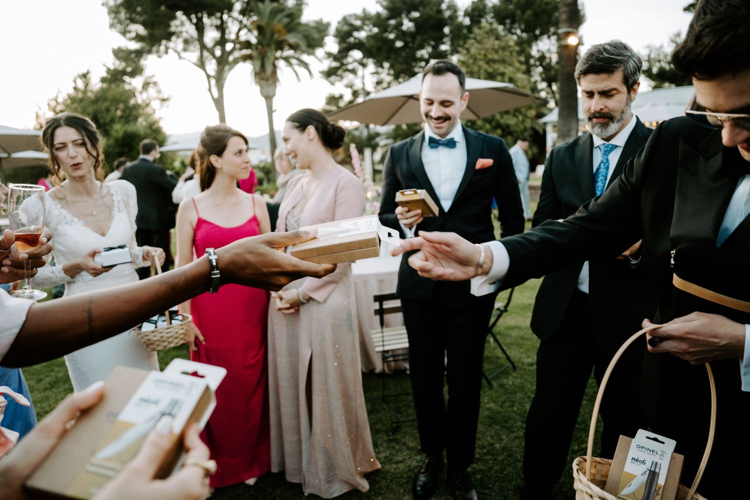 Wedding guests gather outdoors for a celebration under palm trees at dusk.