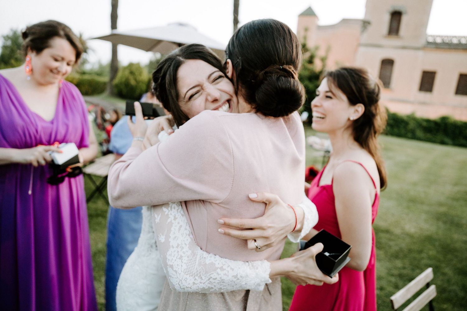 Wedding party members share emotional embraces during an outdoor celebration.