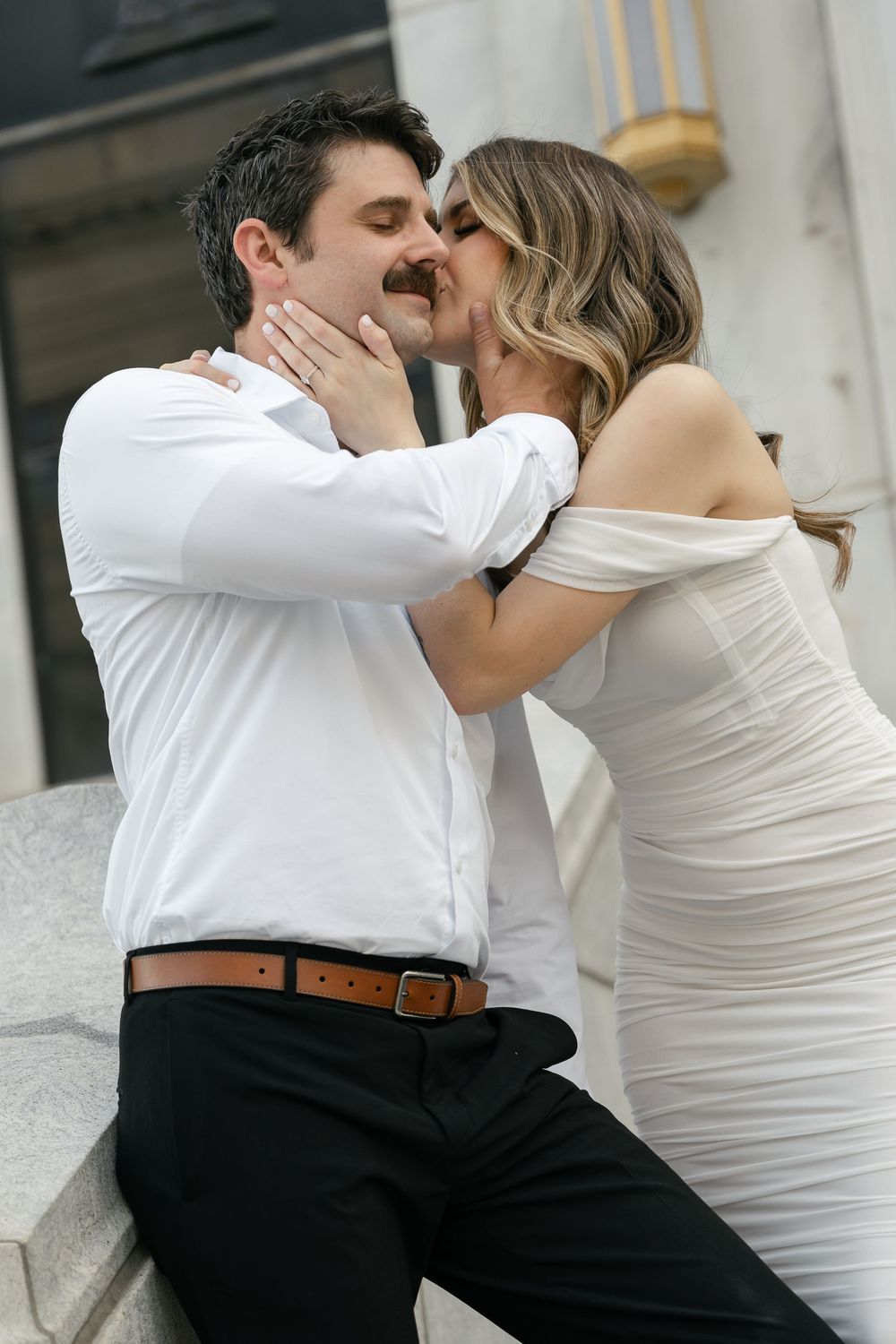 A romantic couple embraces on outdoor steps, with the bride in a white dress and groom in a white shirt and black pants.