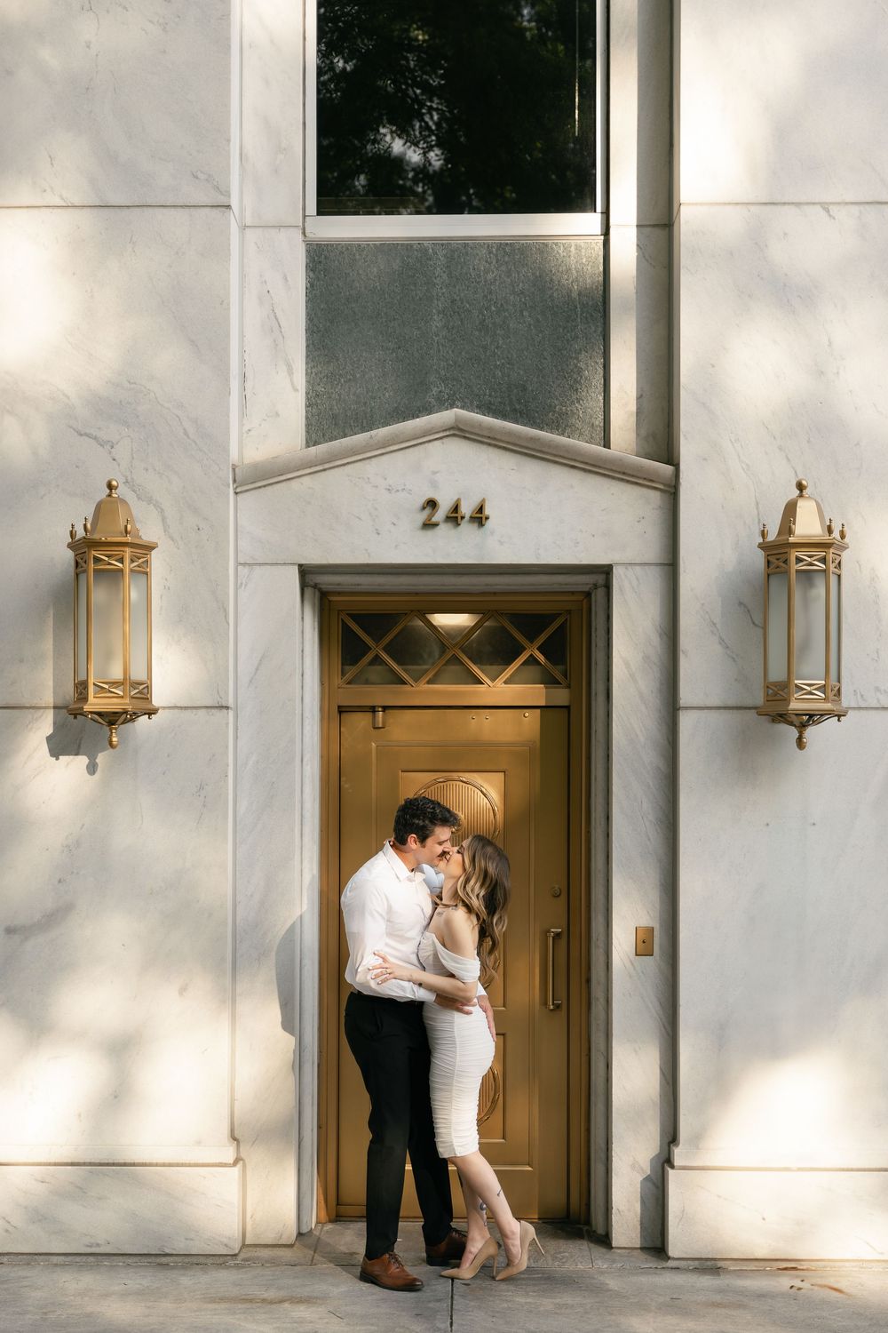 A couple shares a romantic moment in front of an elegant doorway with brass lanterns and the number 244.