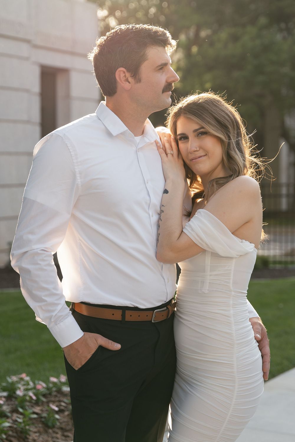 Romantic outdoor wedding photo of couple embracing during golden hour with bride in white dress and groom in dark pants.