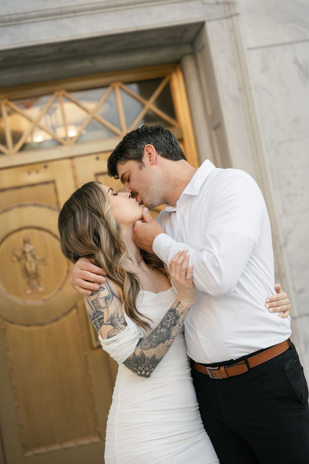 A romantic moment between a couple in wedding attire standing by an ornate door.