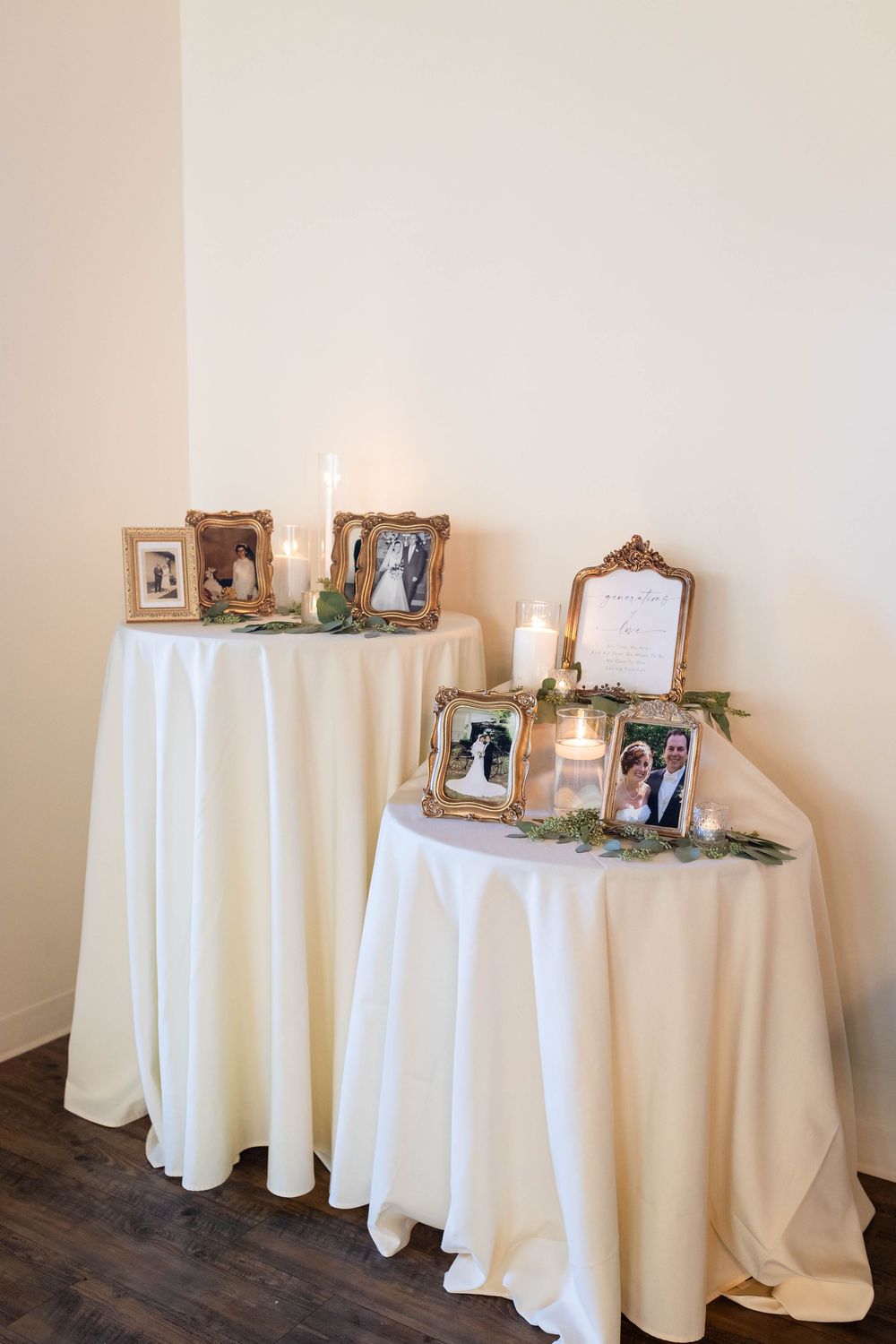 Memorial display with vintage photo frames and candles arranged on two round tables covered in white tablecloths.