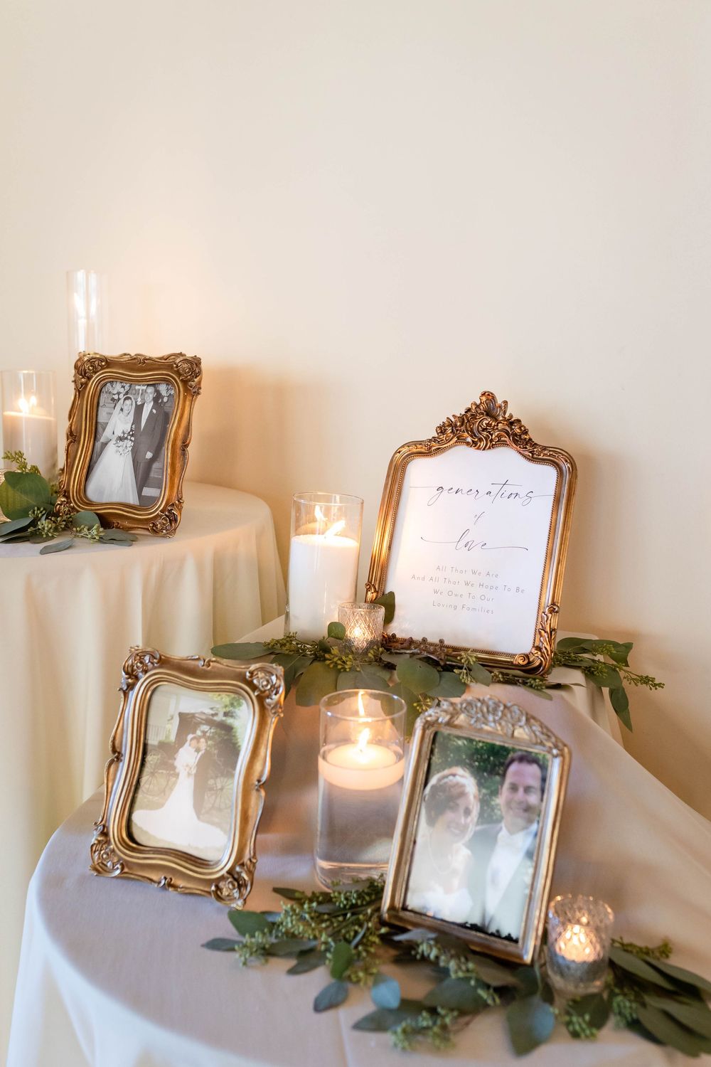 Elegant gold vintage frames with photos displayed on white tablecloth with glowing candles and greenery decorations.