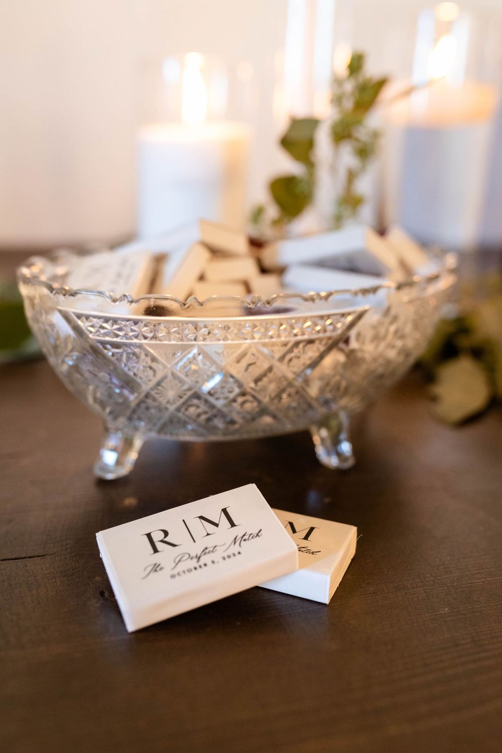 Crystal bowl filled with business cards displayed on dark table with glowing candles and greenery in background.