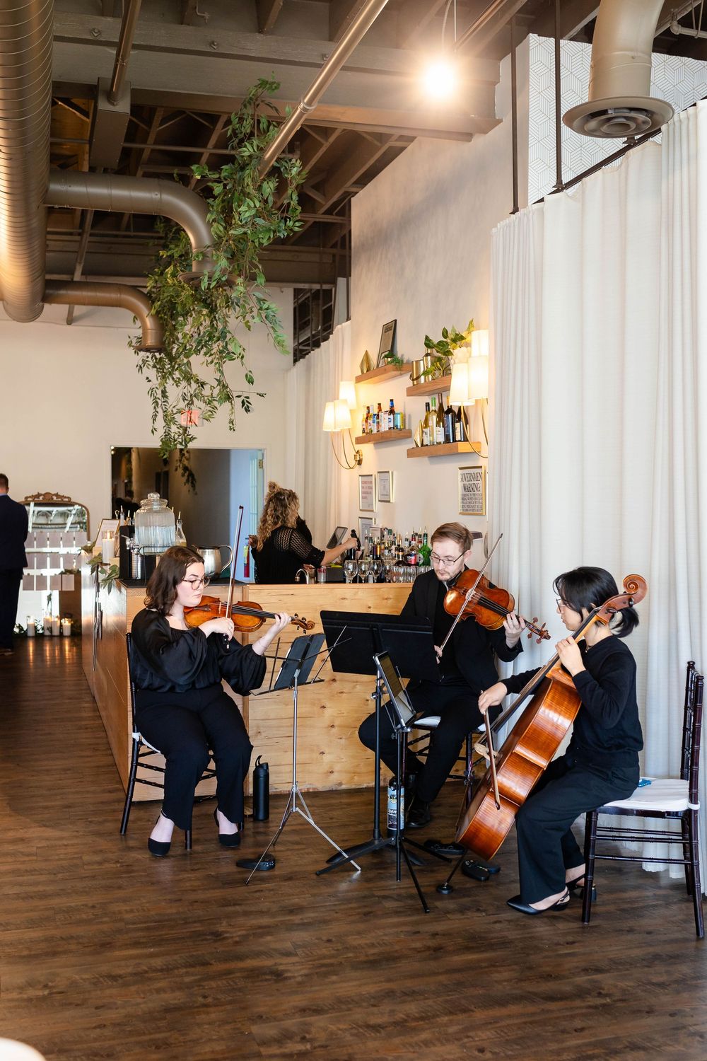 String quartet performs classical music at an industrial-chic venue with exposed ceiling and hanging plants.