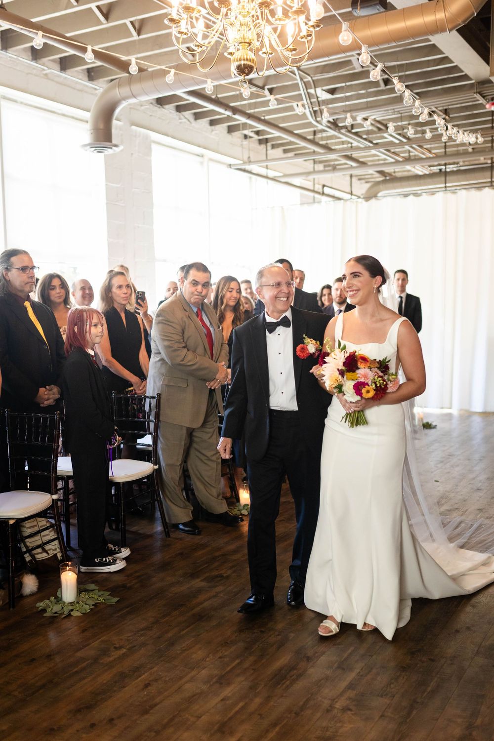 A joyous wedding ceremony moment in an elegant industrial venue with exposed beams and a crystal chandelier.
