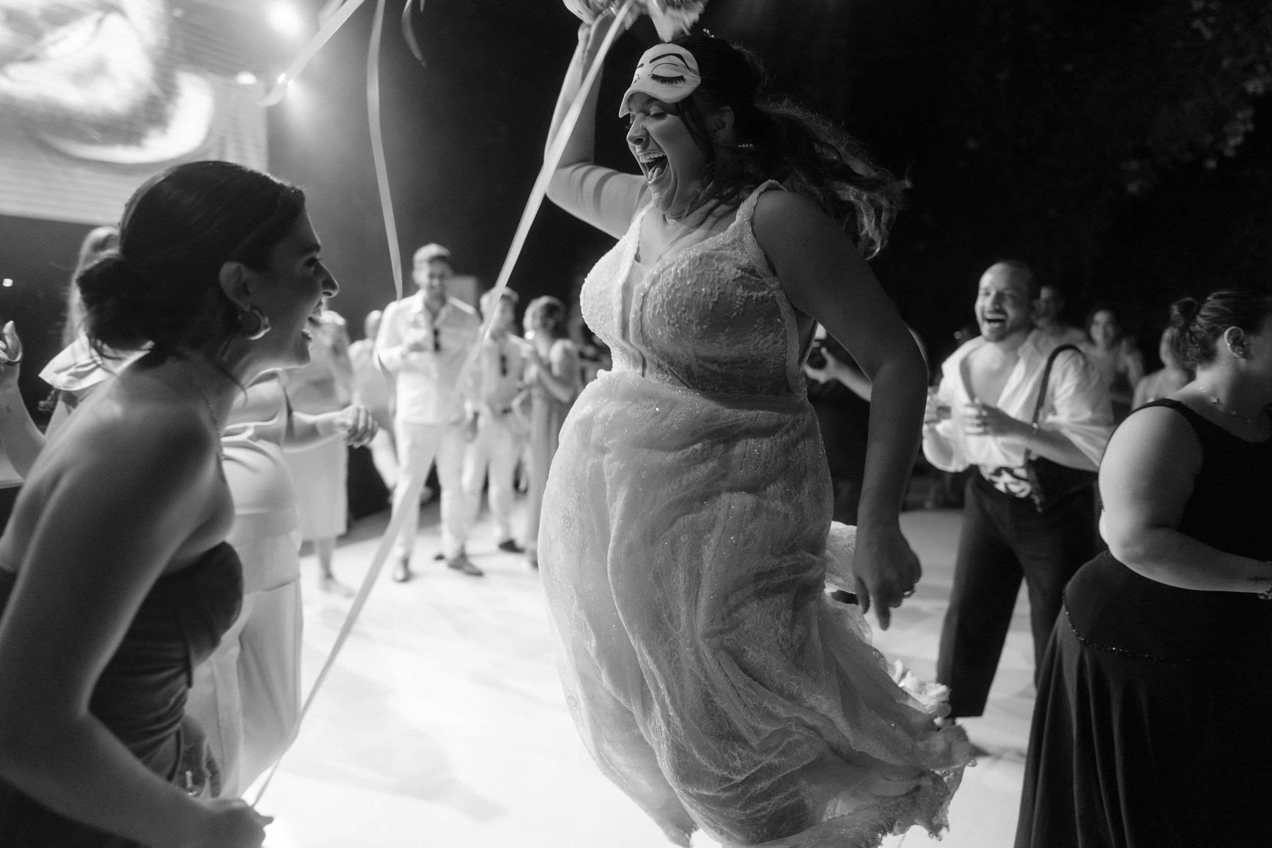 Dancing guests enjoying celebration on illuminated dance floor in black and white photography.