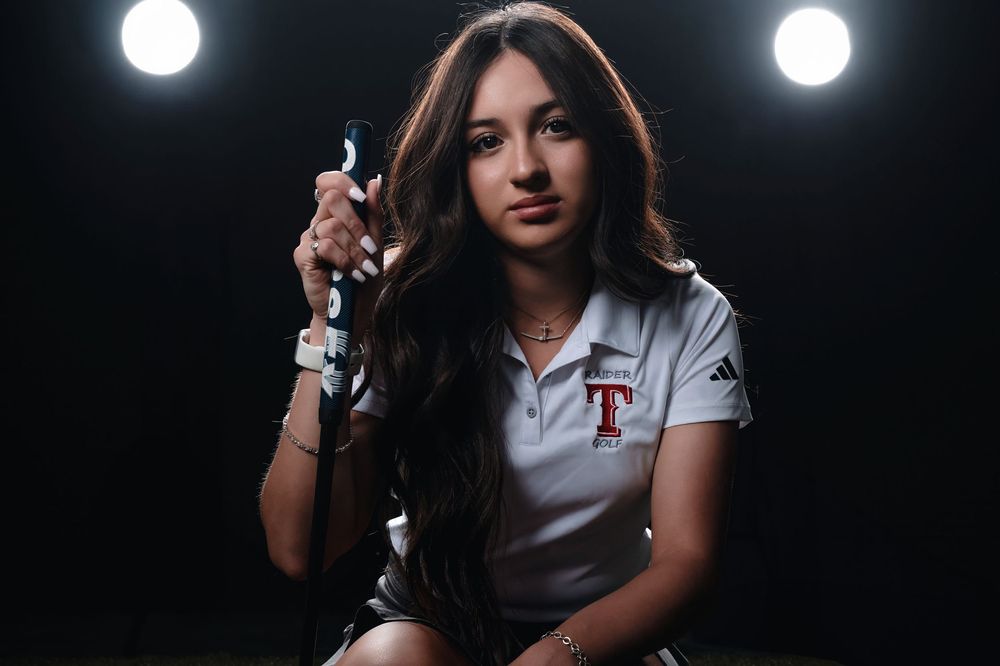 A person in a white Texas Rangers polo sits against a dark background with spotlights shining overhead.