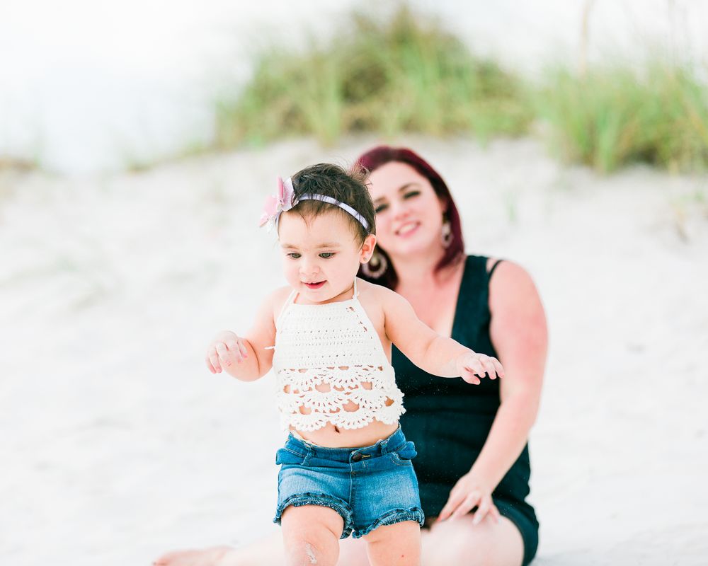 Parent and toddler sitting together on beach dunes in matching outfits.