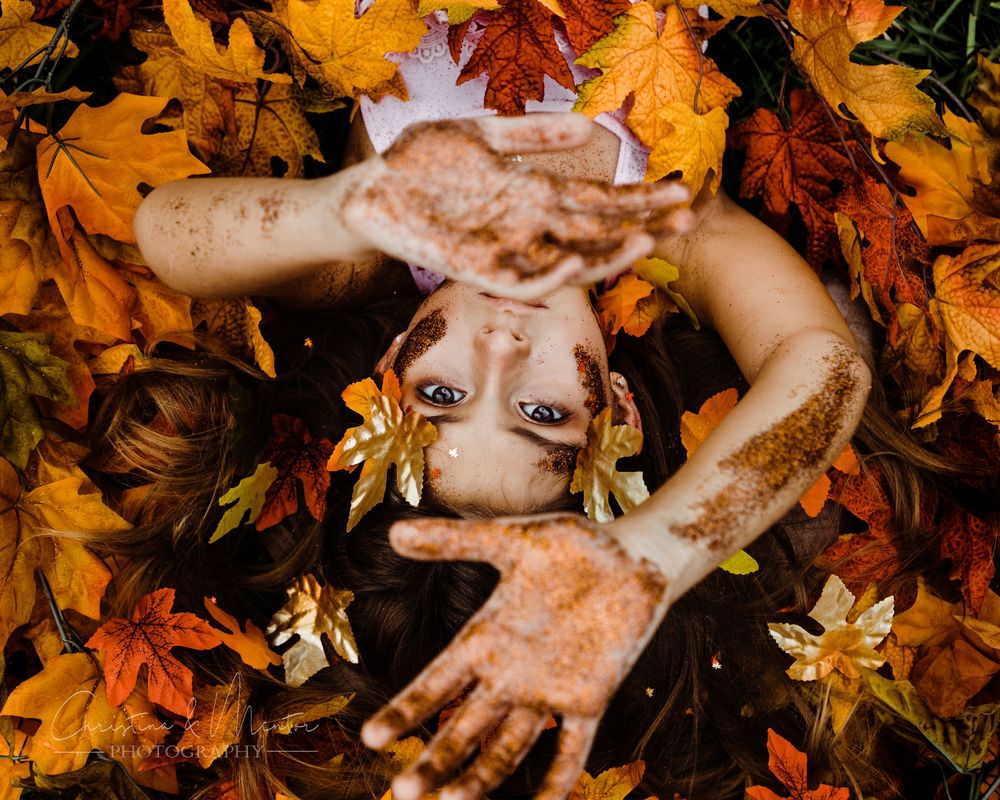 Creative portrait of someone lying in colorful autumn leaves looking up at camera.
