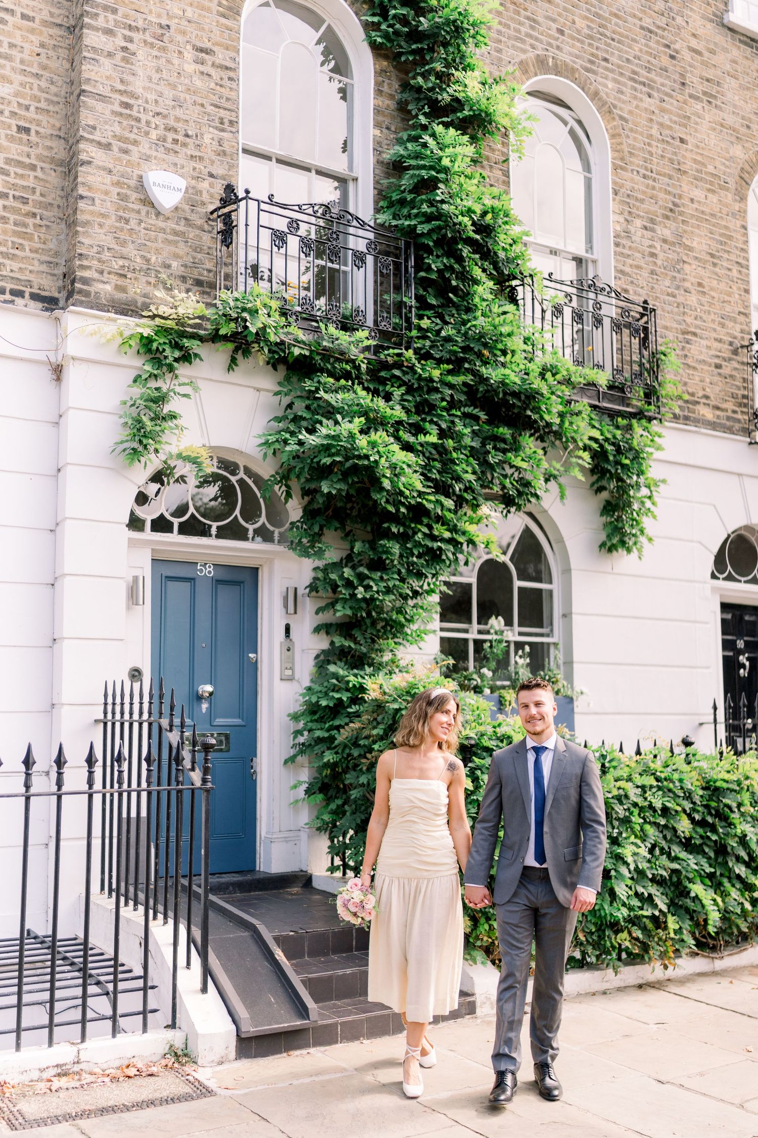 Bride & groom holding hands outside urban London townhouses covered in greenery, sharing a moment in Central London on their wedding day.