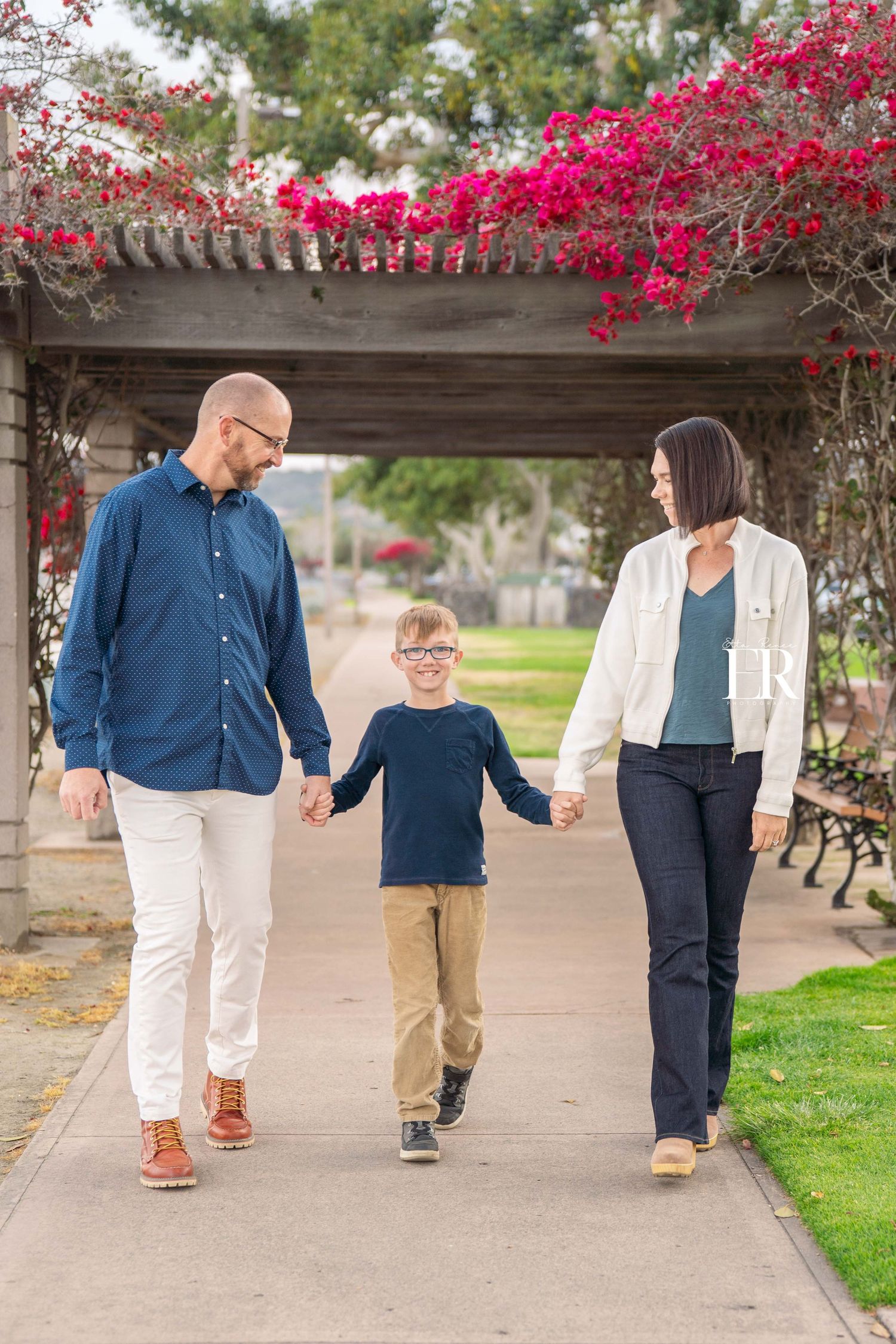 Family walking together under a wooden pergola with bright pink flowers overhead.