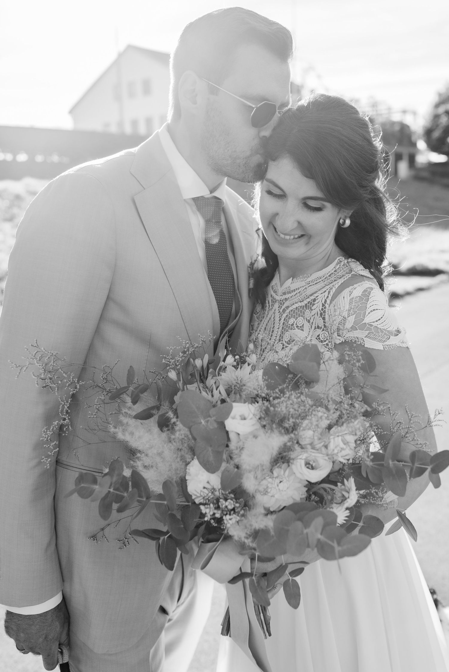 Sun-drenched wedding portrait with elegant bouquet of flowers and greenery.