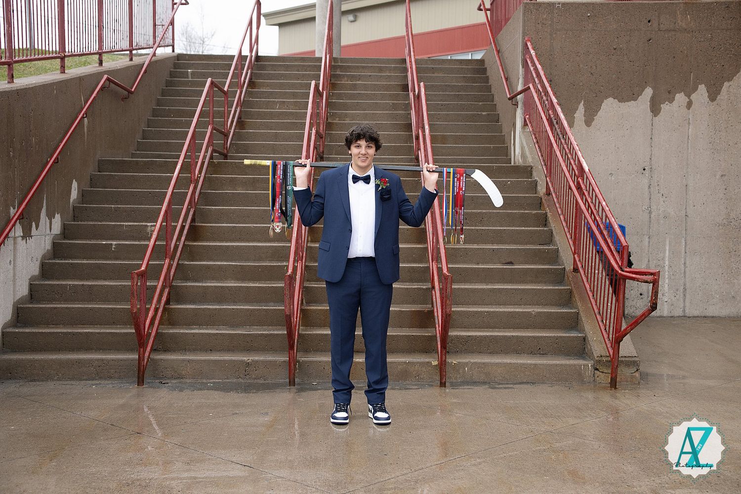 Graduate in navy suit and bowtie poses on concrete staircase with red railings.