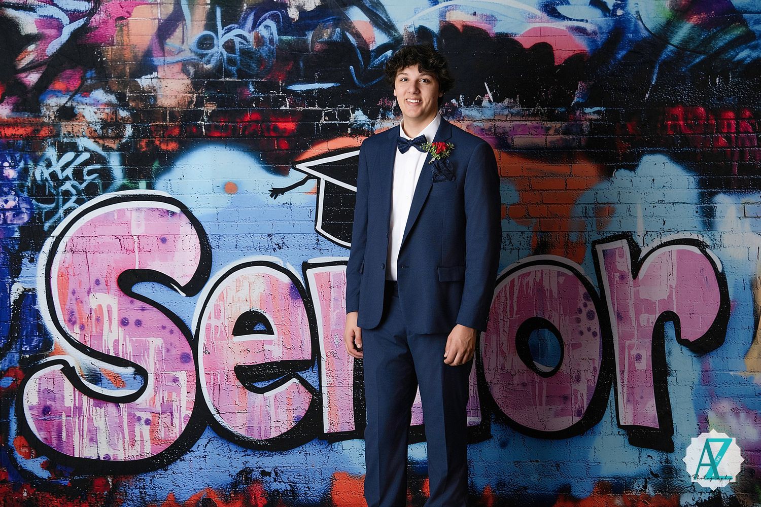 Student portrait taken against vibrant graffiti wall featuring pink 'Senior' text in urban setting.