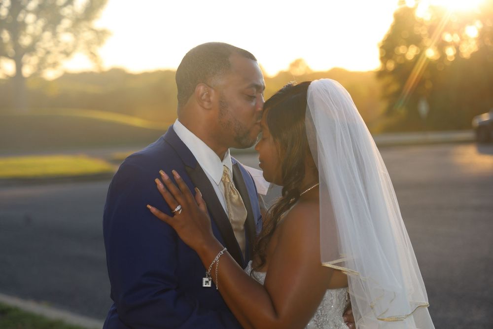 Newlywed couple shares romantic kiss at golden sunset, bride in white veil and groom in navy suit.