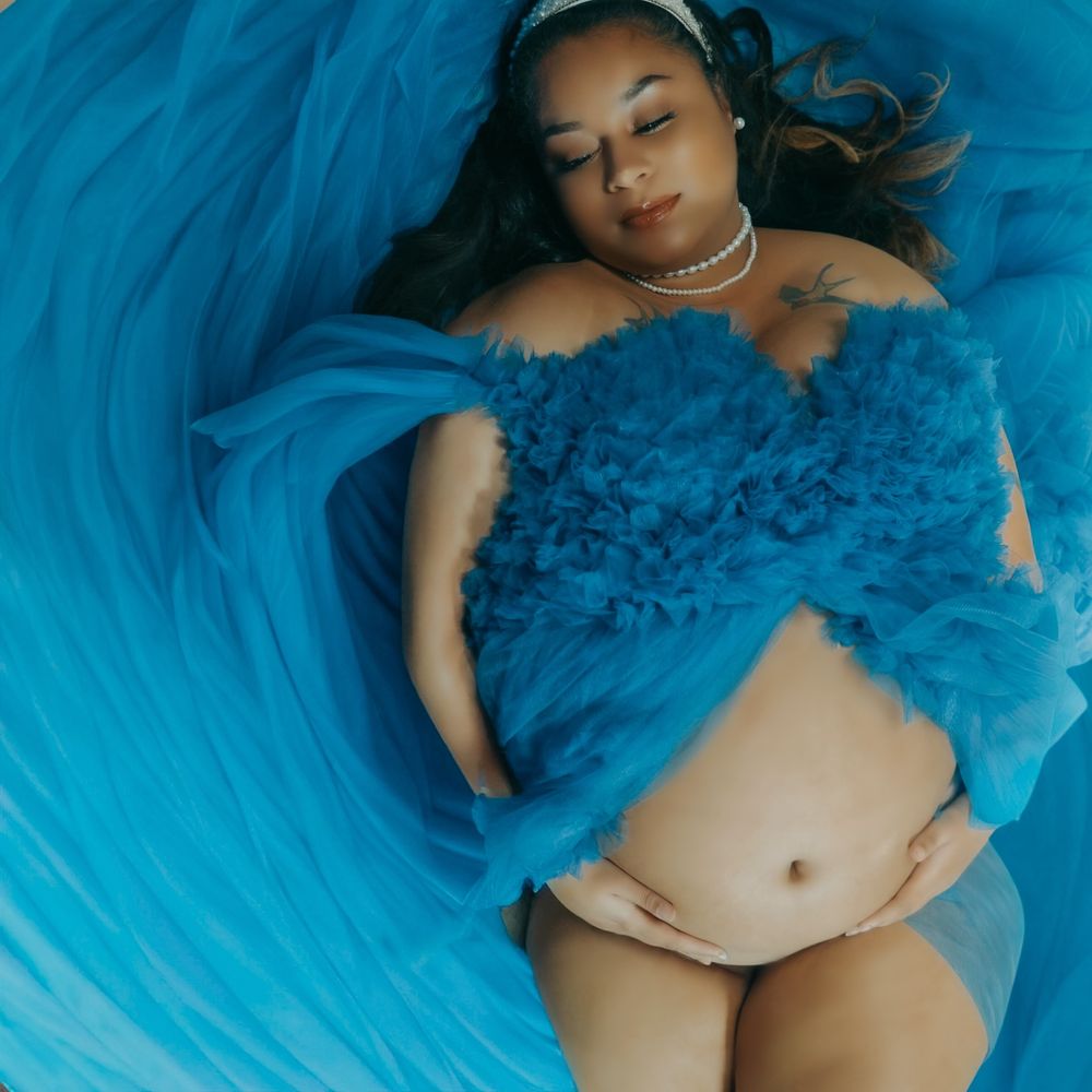 Pregnant woman lying in flowing blue tulle fabric for artistic aerial maternity photography session.