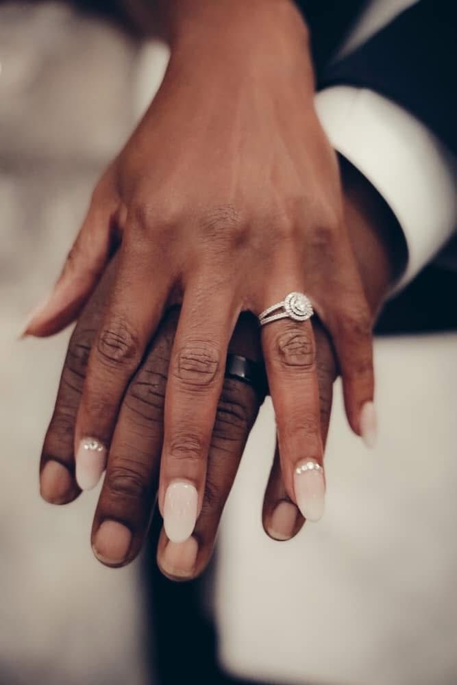 Close-up of newlywed couple's hands displaying diamond engagement ring and wedding bands.