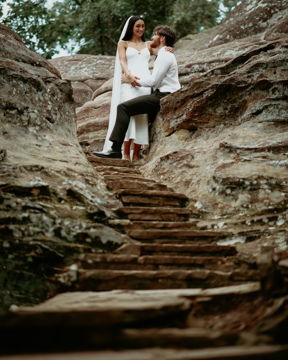 A bride and groom embrace on rustic stone steps carved into red rock formations during an outdoor wedding elopement.