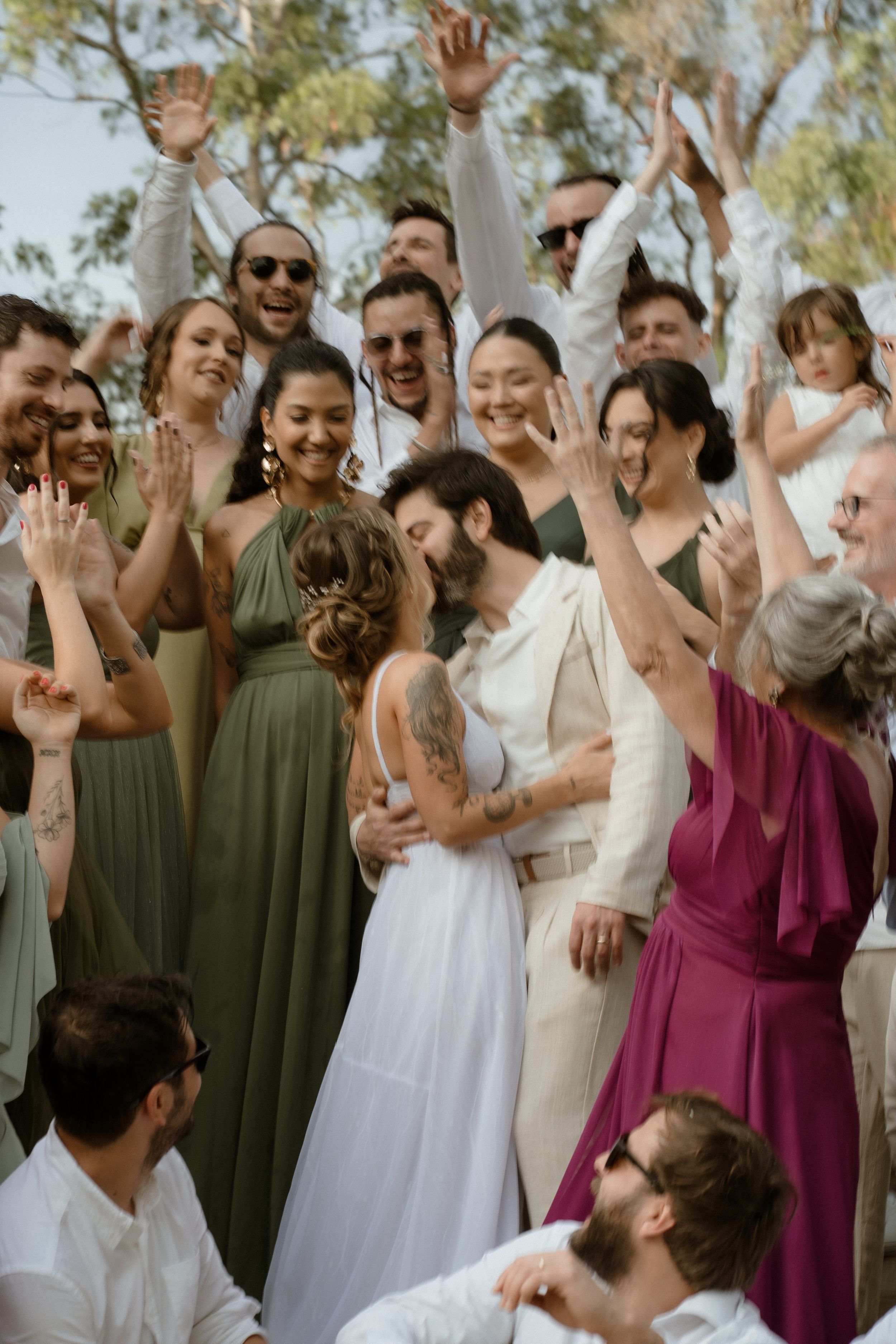 Wedding party celebrating with raised hands and joyful expressions in the afternoon sunlight.