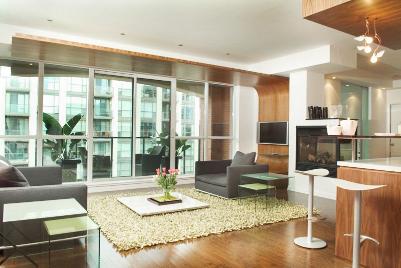 Modern open concept condo living room with floor-to-ceiling windows, leather sofas and area rug in an urban high-rise.