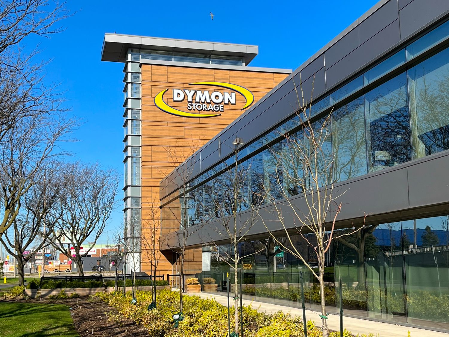 Modern commercial building with Dymon logo on wood-paneled wall exterior and large glass windows under blue sky.