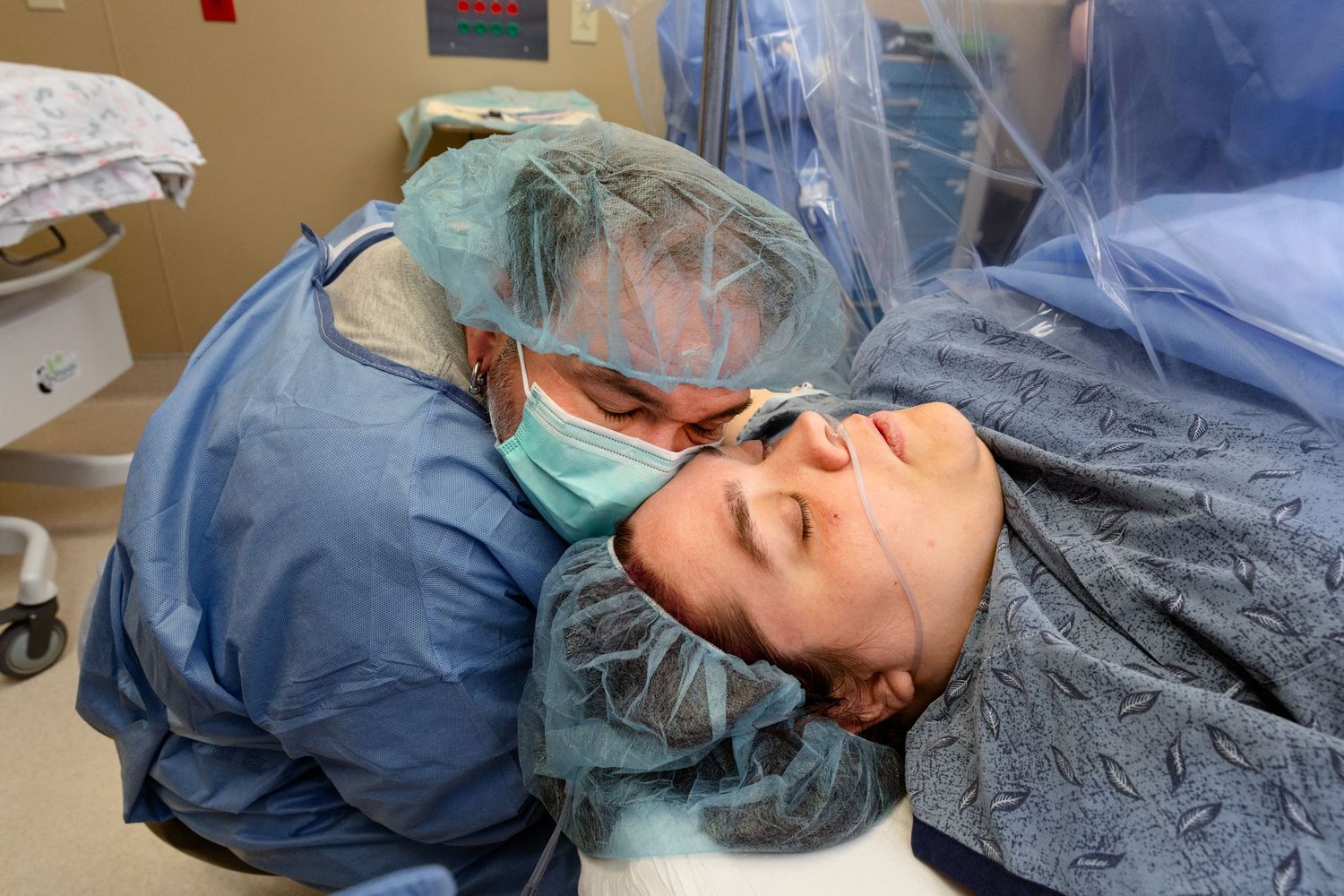 A mother being supported by her baby's father in the OR during a cesarean section birth. Both are wearing hospital gowns.