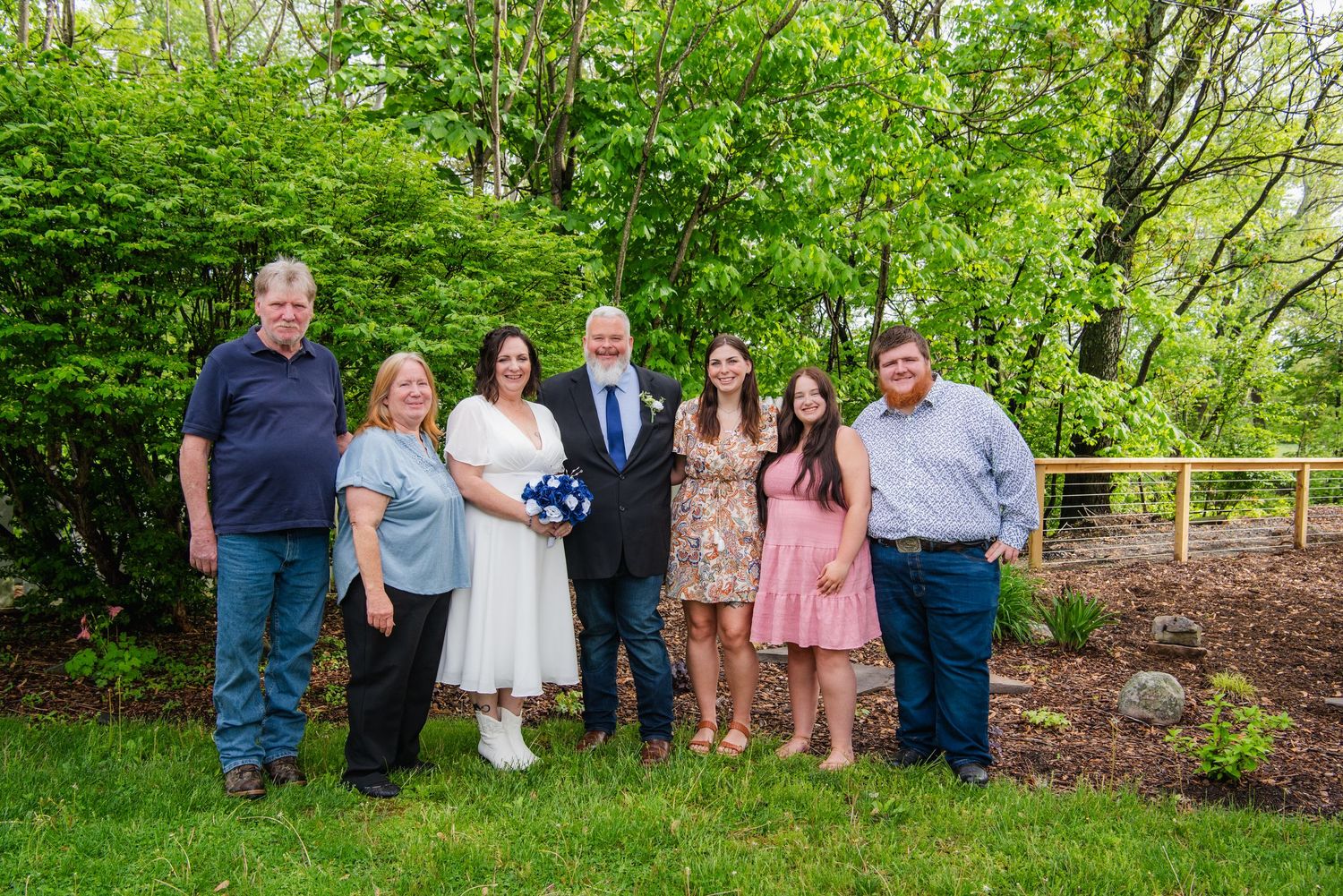 A small wedding party poses together on a garden path surrounded by greenery.