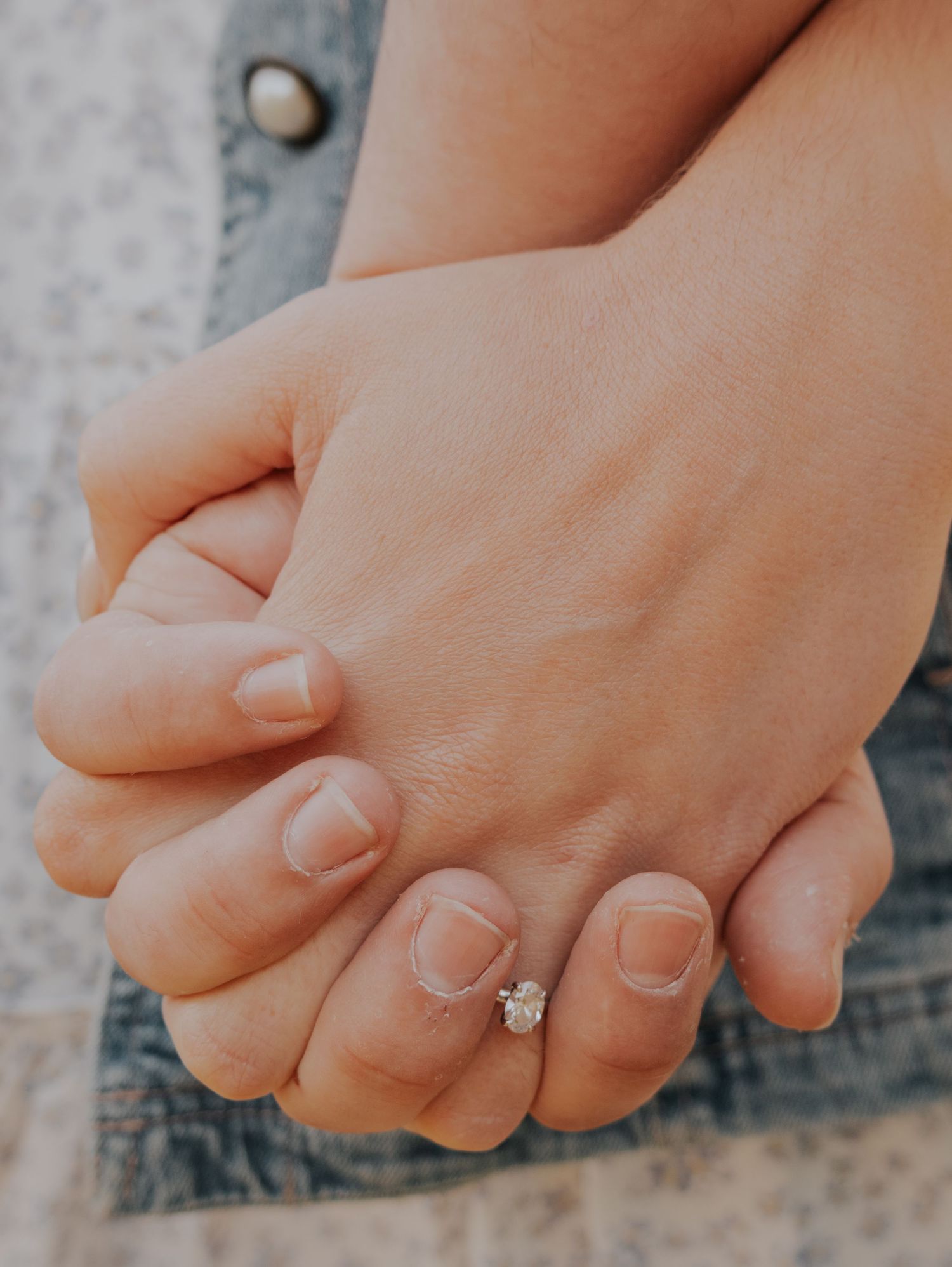 Close-up of two hands clasped together with an engagement ring featuring a delicate diamond solitaire.
