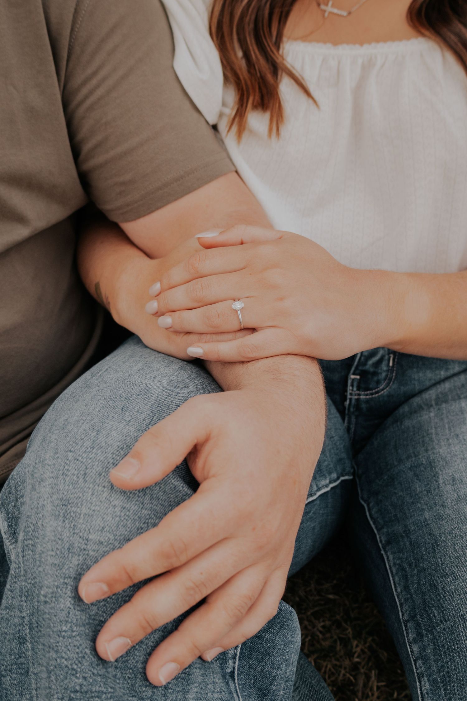 Close-up view of hands embracing over jeans, with a white top and brown shirt showing tender affection.