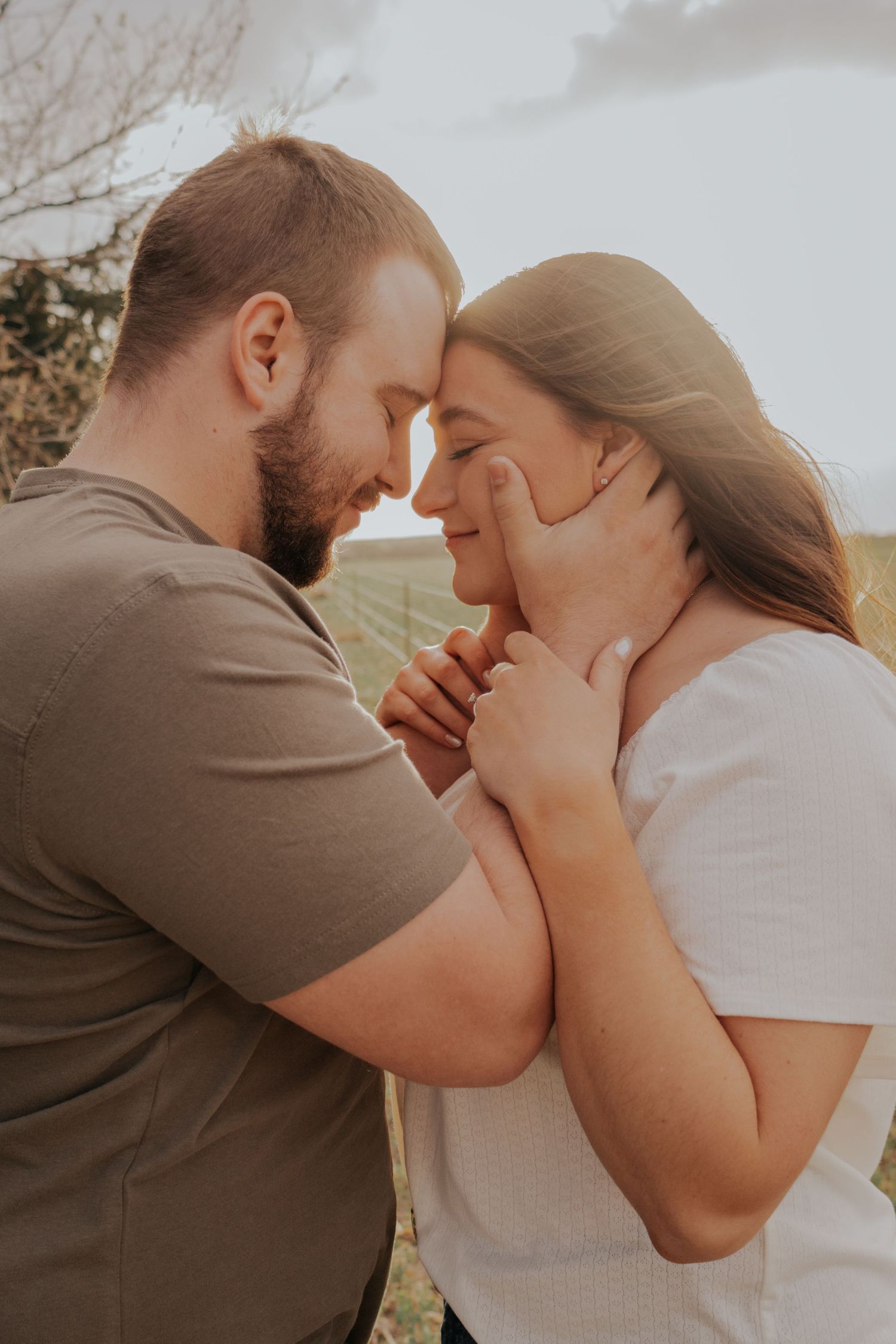 Intimate portrait of romantic couple embracing in warm sunlight with tender expressions and gentle touch.