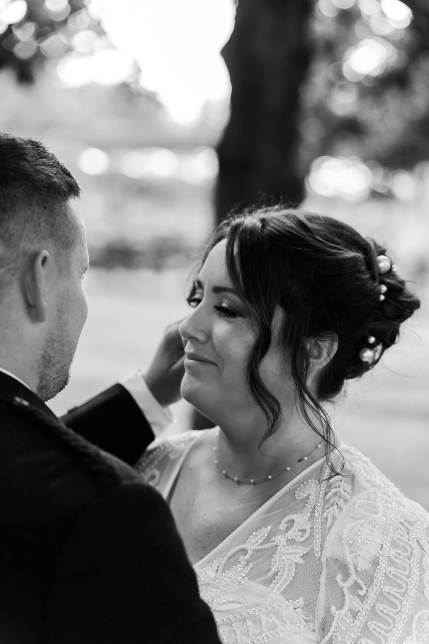 A tender black and white wedding portrait capturing a romantic moment between newlyweds with bokeh background.