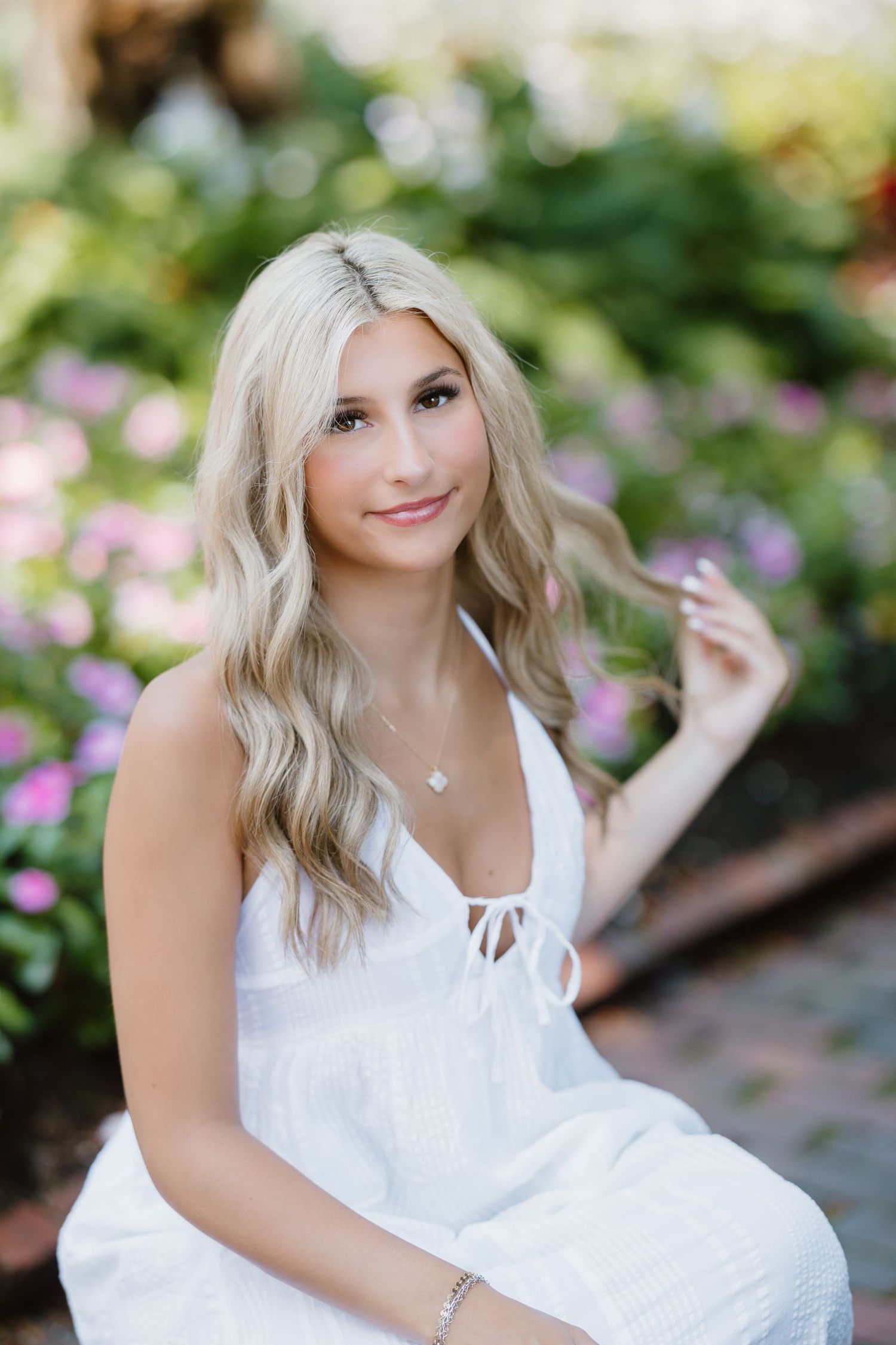 A young woman in a white top poses outdoors in a field with natural lighting and a bright, genuine smile.