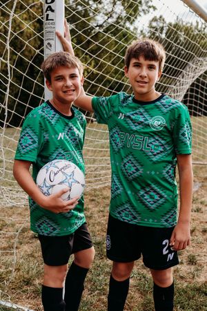 Young soccer players wearing green jerseys and black shorts pose by a goal net during practice.