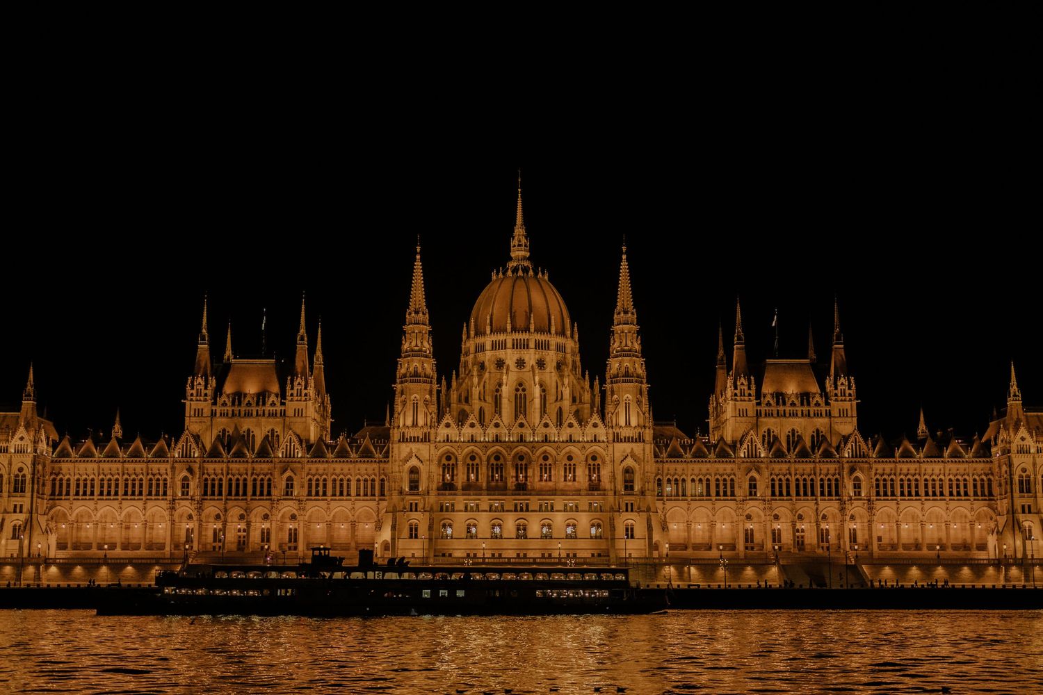 The Hungarian Parliament Building illuminated at night reflects golden light on the Danube River in Budapest.