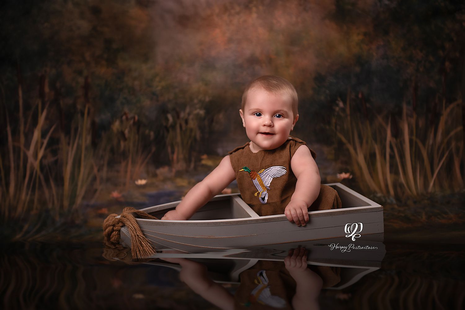 Artistic photo of baby boy sitting in boat with water and fine art backdrop; best photographer Lexington, SC; fine art painterly portrait