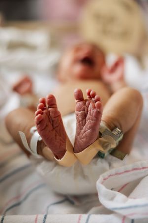 Close-up view of tiny newborn baby feet with wrinkled pink skin resting on white fabric.