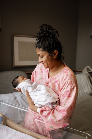 A tender moment in a hospital room as a mother in pink holds her swaddled newborn baby.
