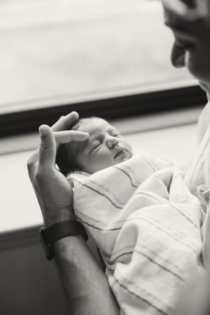 A tender black and white portrait of a tiny newborn being gently cradled in adult hands.