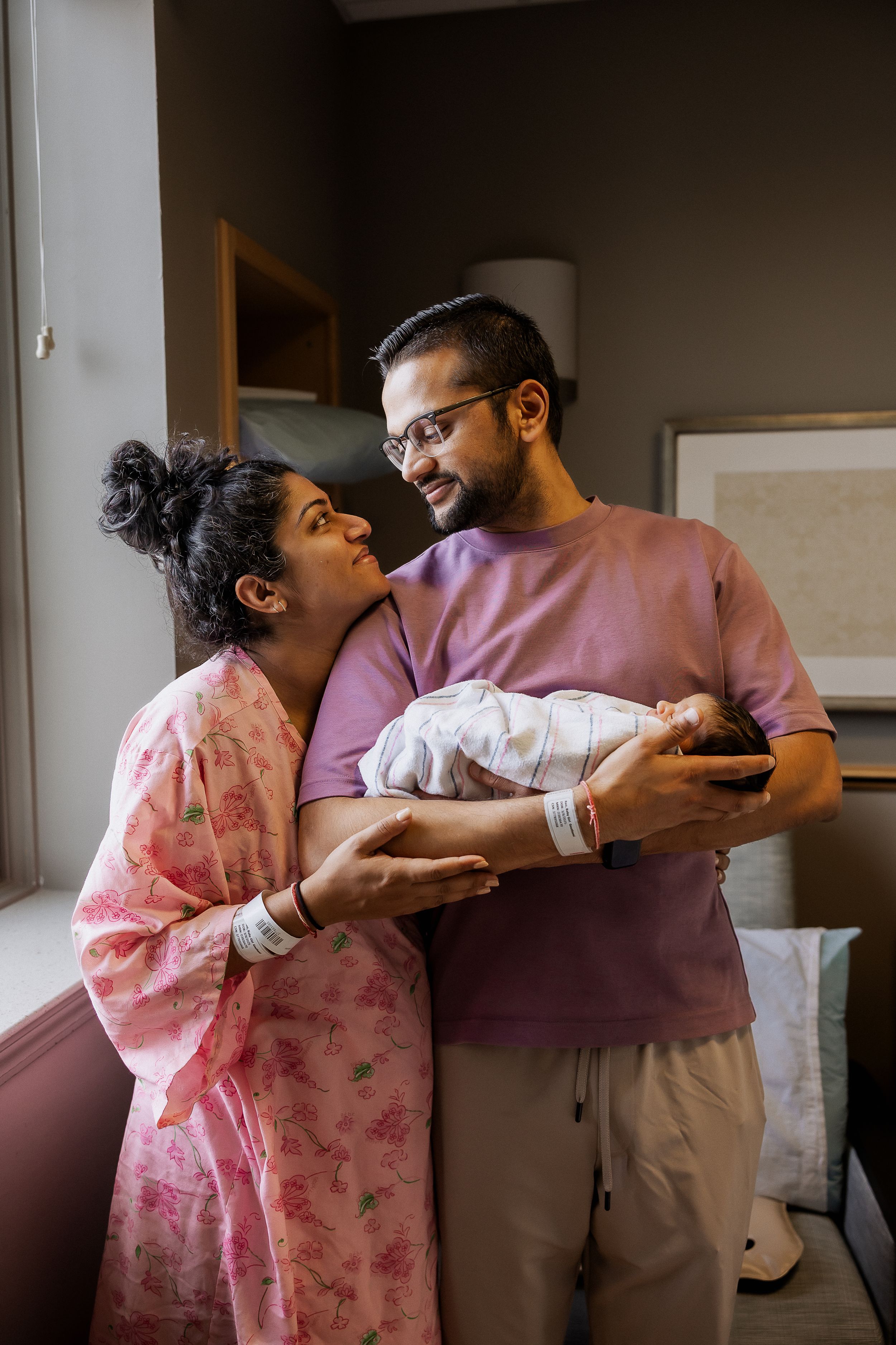 A tender moment as new parents gaze lovingly at their newborn baby in a hospital room.