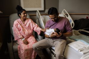 Parents in a hospital room admire their newborn baby while wearing casual clothing.