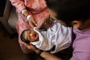 A swaddled newborn baby lies cradled in someone's arms while receiving care at a medical facility.