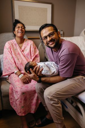 A joyful moment in a hospital room as new parents share smiles while holding their newborn baby.